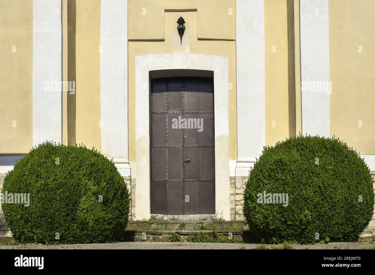 Cespugli in bosso Evergreen (Buxus) a forma di palla vicino alla porta di metallo, l'ingresso al vecchio edificio della Chiesa cattolica. Copia spazio. Sele Foto Stock