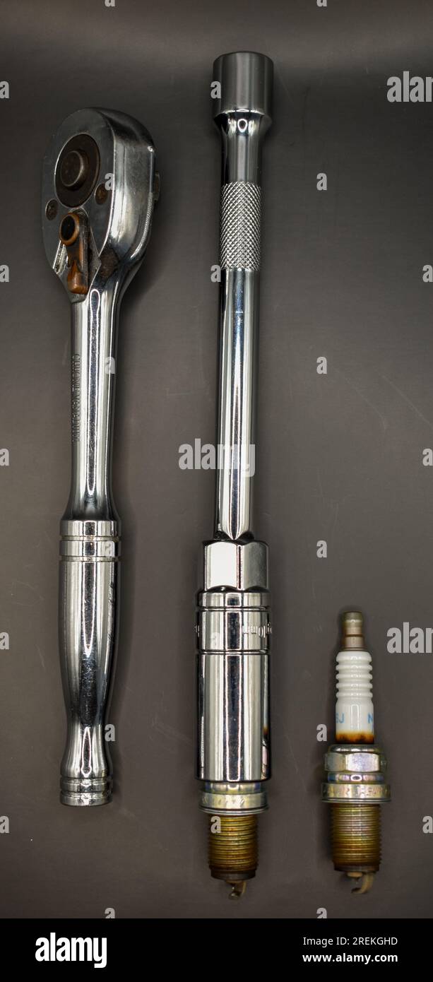 Una chiave a bussola, una barra di prolunga con una chiave a bussola collegata e due candele usate fotografate su uno sfondo scuro. Foto Stock