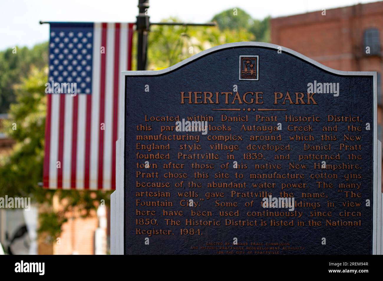 Prattville, Alabama, Stati Uniti d'America - 16 giugno 2023: Cartello informativo storico per l'Heritage Park nel centro storico di Prattville con sullo sfondo la bandiera americana. Foto Stock
