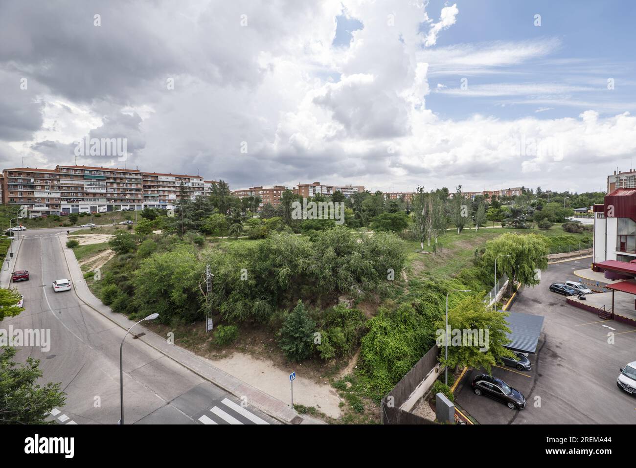 Bellissime aree paesaggistiche di un parco urbano con siepi, alberi ed erba circondate da strade, parcheggi ed edifici Foto Stock