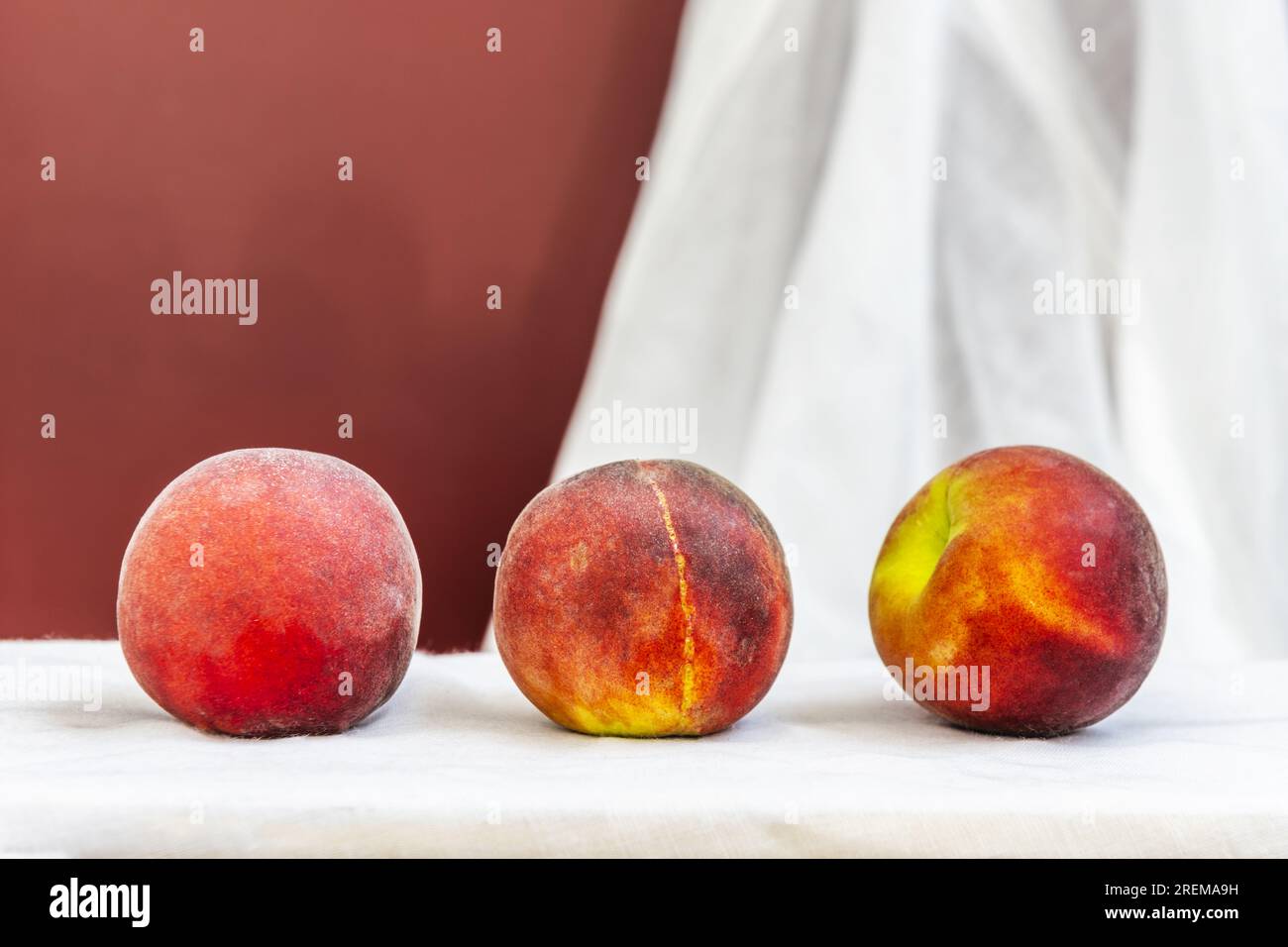 Alcune pesche rosse maturano in linea su un panno bianco Foto Stock