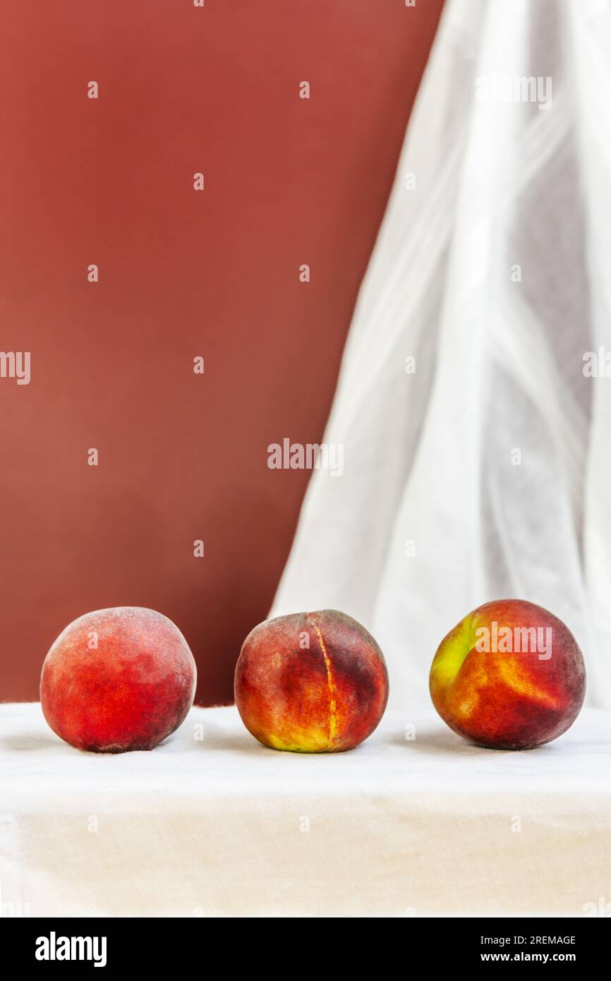 Alcune pesche rosse maturano in linea su un panno bianco appeso al muro Foto Stock