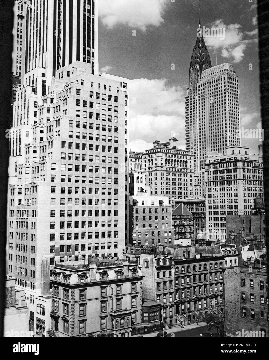 New York, New York: c. 1940 New York City vista da Madison Avenue con il famoso Chrysler Building sullo sfondo. I grattacieli contrastano con gli edifici più piccoli degli appartamenti e con le loro iconiche piazze di fronte. Foto Stock