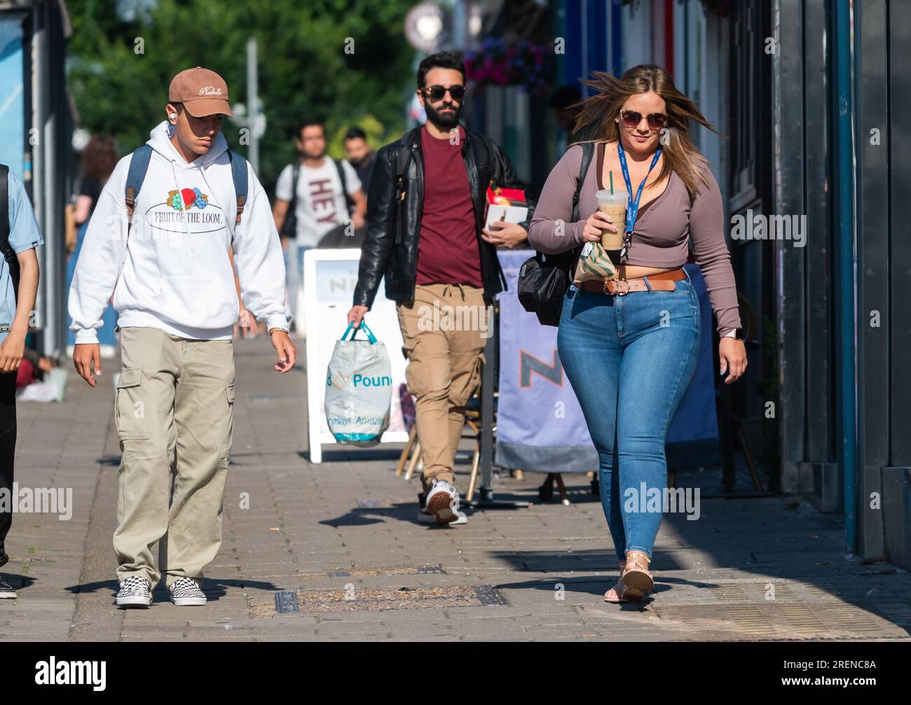 Bella giovane donna che indossa jeans in denim, vestita alla moda, cammina in città trafficata con drink da asporto, con borsa a spalla, in estate, Regno Unito. Foto Stock