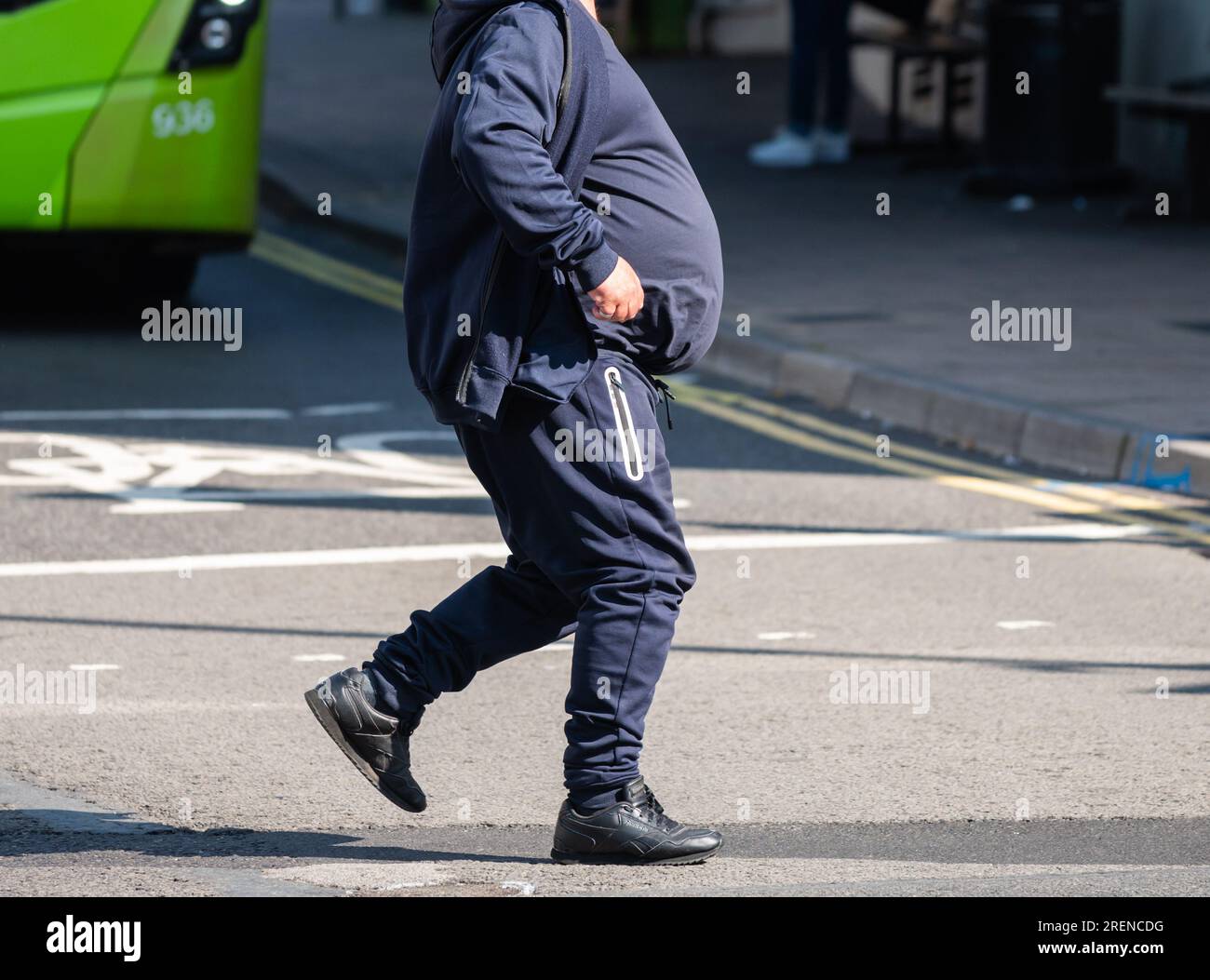 Uomo in sovrappeso con pancia grande o pancia grande, senza mostrare la testa, camminando attraverso una strada, Regno Unito. Uomo obeso. Foto Stock