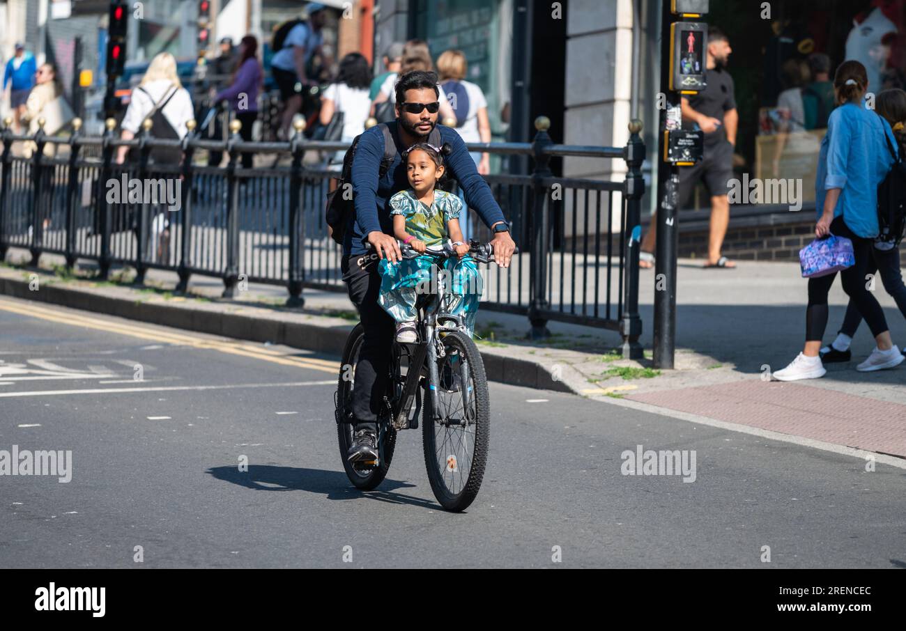 Uomo e bambino in bicicletta insieme su una strada principale, senza casco. Ciclista senza casco nel Regno Unito. Sicurezza dei bambini. Foto Stock