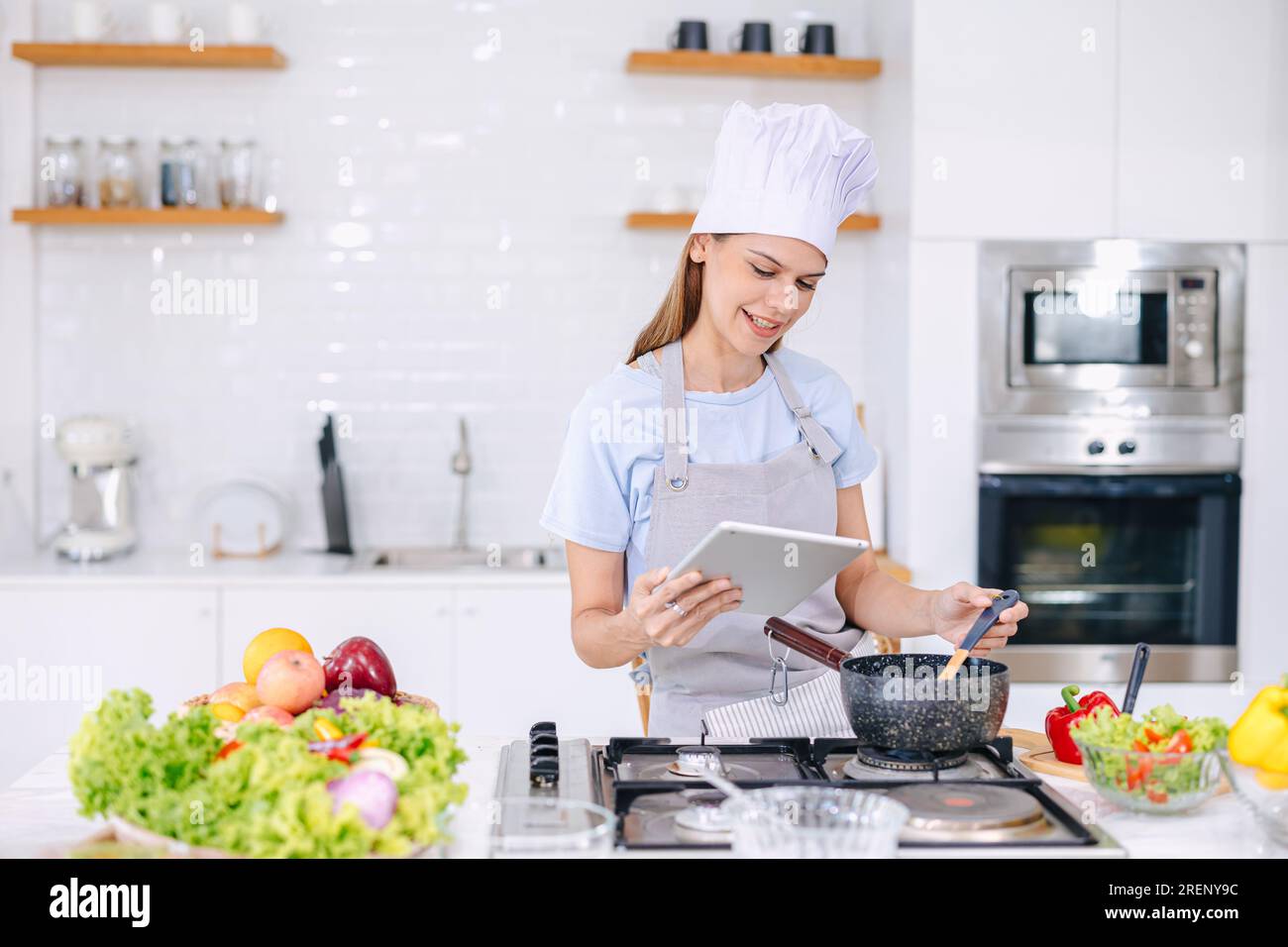 donna felice godere cucinare il cibo in cucina a casa imparare verdure sane cucinare guardando online classe internet video in tablet Foto Stock