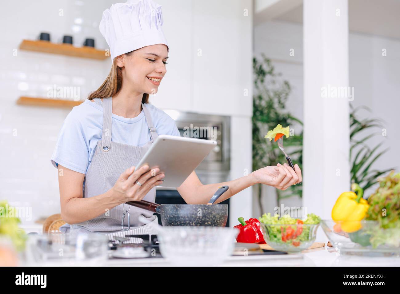 Bel modello donna felice cibo sano cucina insalata di verdure in cucina con tablet online Foto Stock