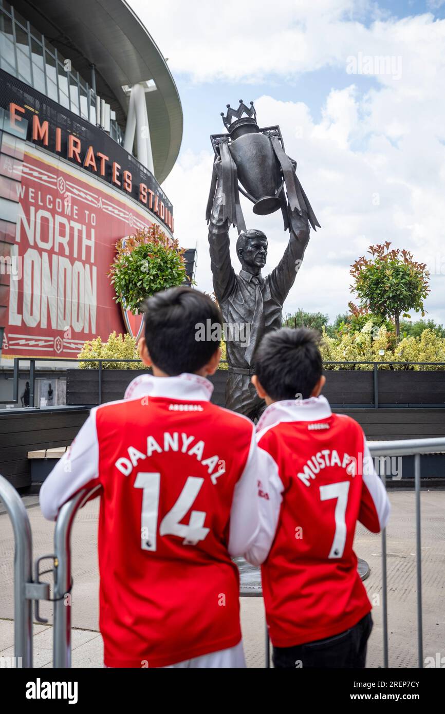 Londra, Regno Unito. 29 luglio 2023. I giovani tifosi vedono la statua del manager dell'Arsenal Arsène Wenger che detiene il trofeo della Premier League che è stato installato all'esterno dell'Emirates Stadium il giorno precedente. Il leggendario allenatore guidò l'Arsenal FC a tre titoli di Premier League, tra cui la famosa stagione degli Invincibles nel 2003/04, dove la sua squadra rimase imbattuta, e sette fa Cup. Creata dallo scultore Jim Guy, la statua di bronzo è alta 3,5 m e pesa quasi mezza tonnellata. [Permesso concesso] credito: Stephen Chung / Alamy Live News Foto Stock