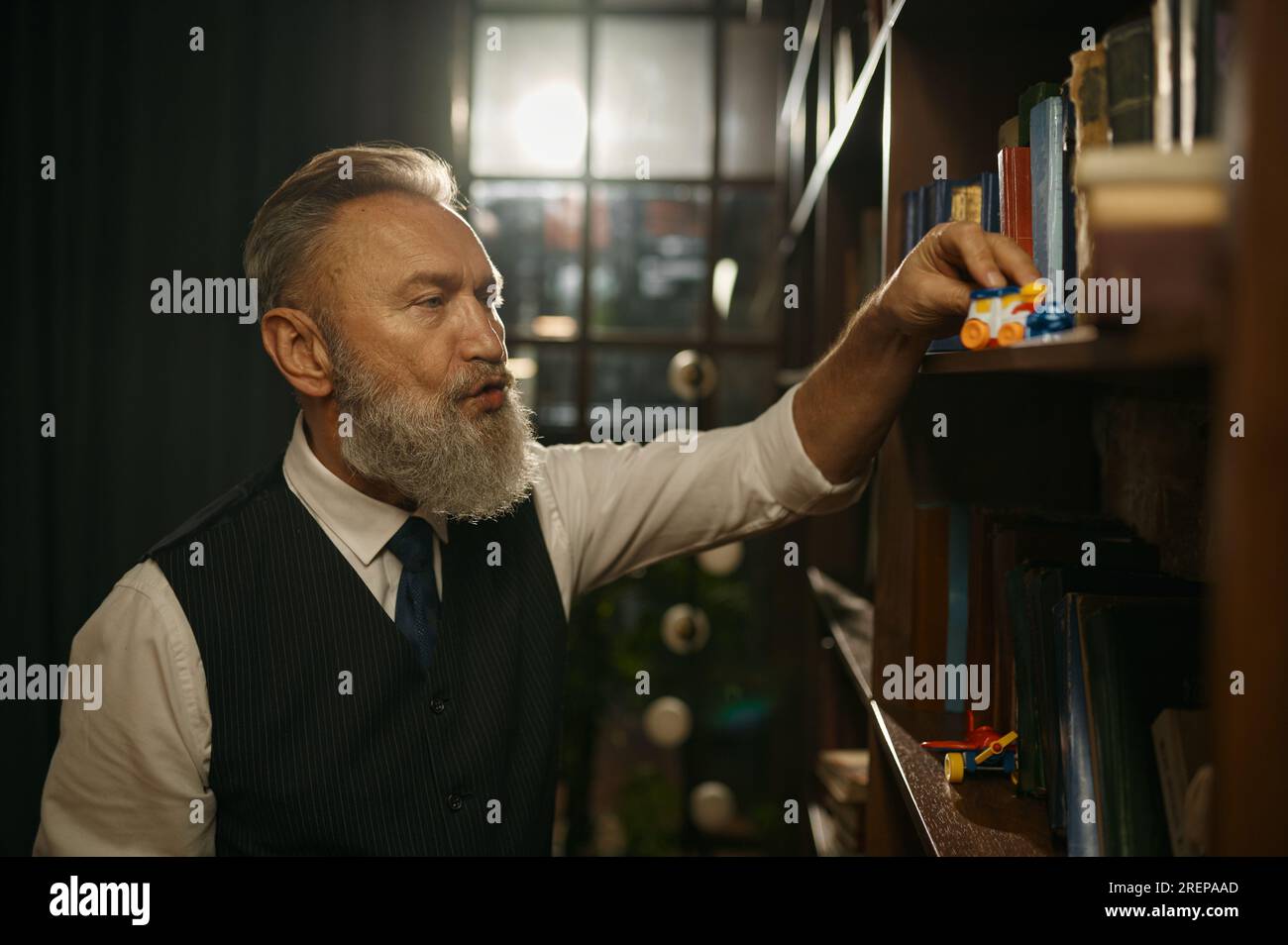 Uomo d'affari anziano con un vestito vecchio stile che gioca a giocattoli in biblioteca Foto Stock