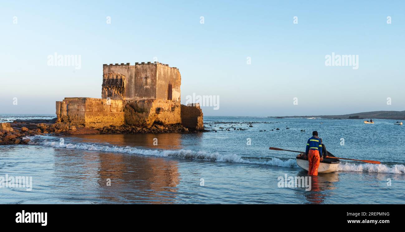 I pescatori che spingono la loro piccola barca tra le onde di una pausa costiera Foto Stock