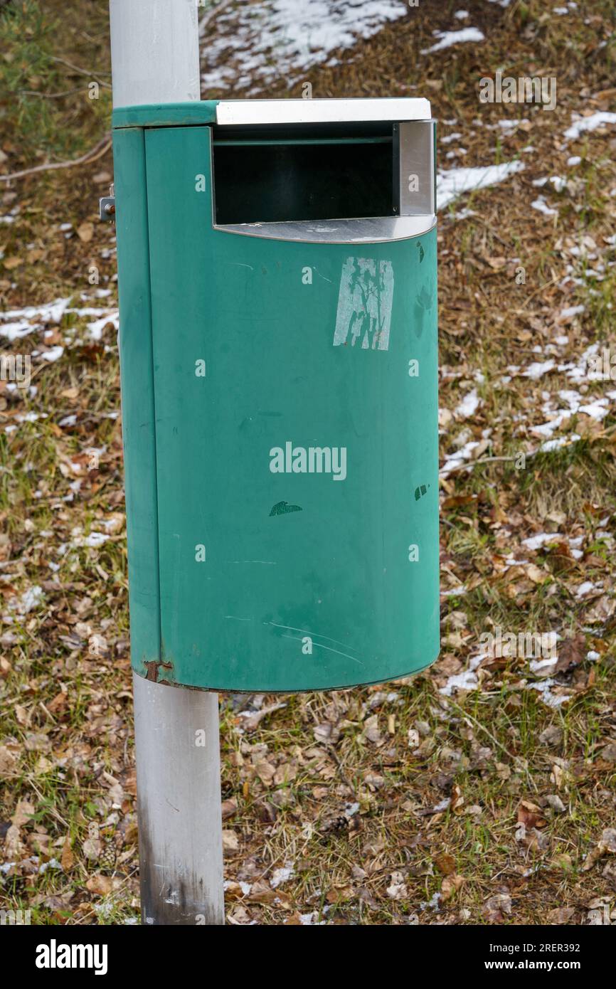 Cestino verde può su palo metallico con erba e neve sullo sfondo Foto Stock