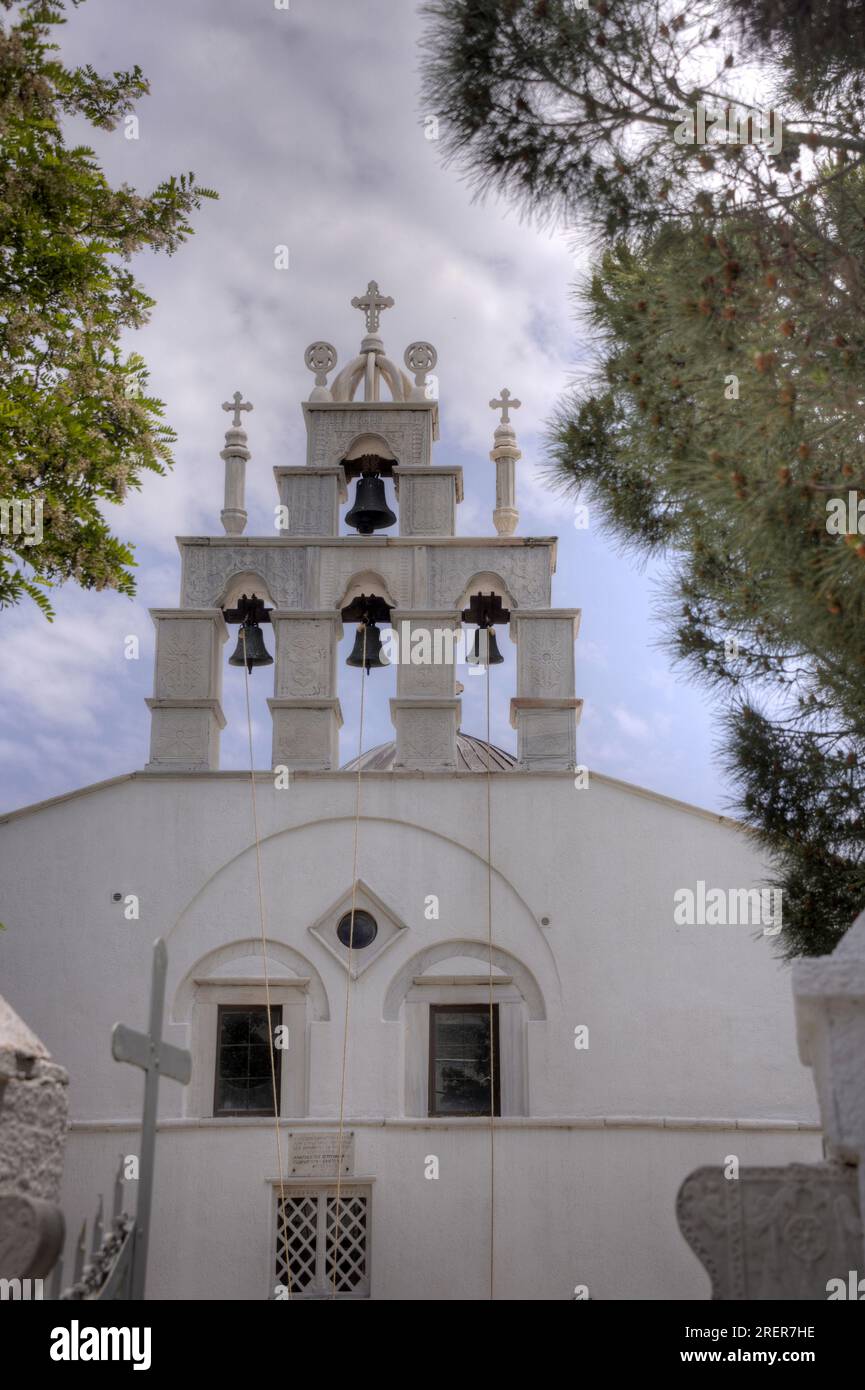 Campanile di una chiesa greco-ortodossa in un villaggio sull'isola di Naxos, Grecia. Incorniciato da alberi contro un cielo leggermente nuvoloso. Foto Stock