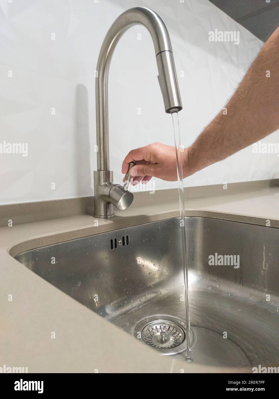 Mano maschio che apre il rubinetto del lavandino della cucina. Messa a fuoco selettiva Foto Stock