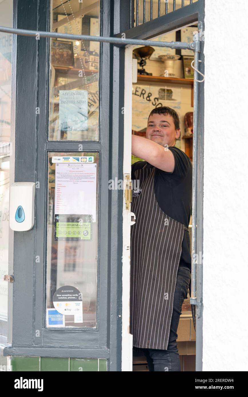 Un macellaio che indossa un grembiule sta organizzando la selezione della carne nel refrigeratore del negozio. Ledbury DT Wallers and Sons Foto Stock