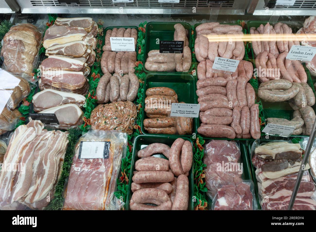 Un macellaio che indossa un grembiule sta organizzando la selezione della carne nel refrigeratore del negozio. Ledbury DT Wallers and Sons Foto Stock