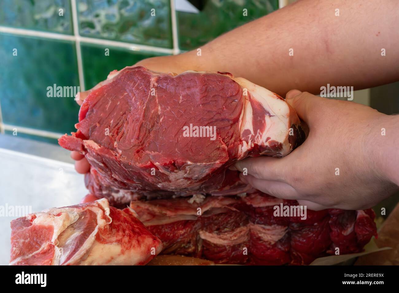 In un negozio vicino c'è un macellaio che tiene in mano un taglio di striploin di manzo di alta qualità. Foto Stock
