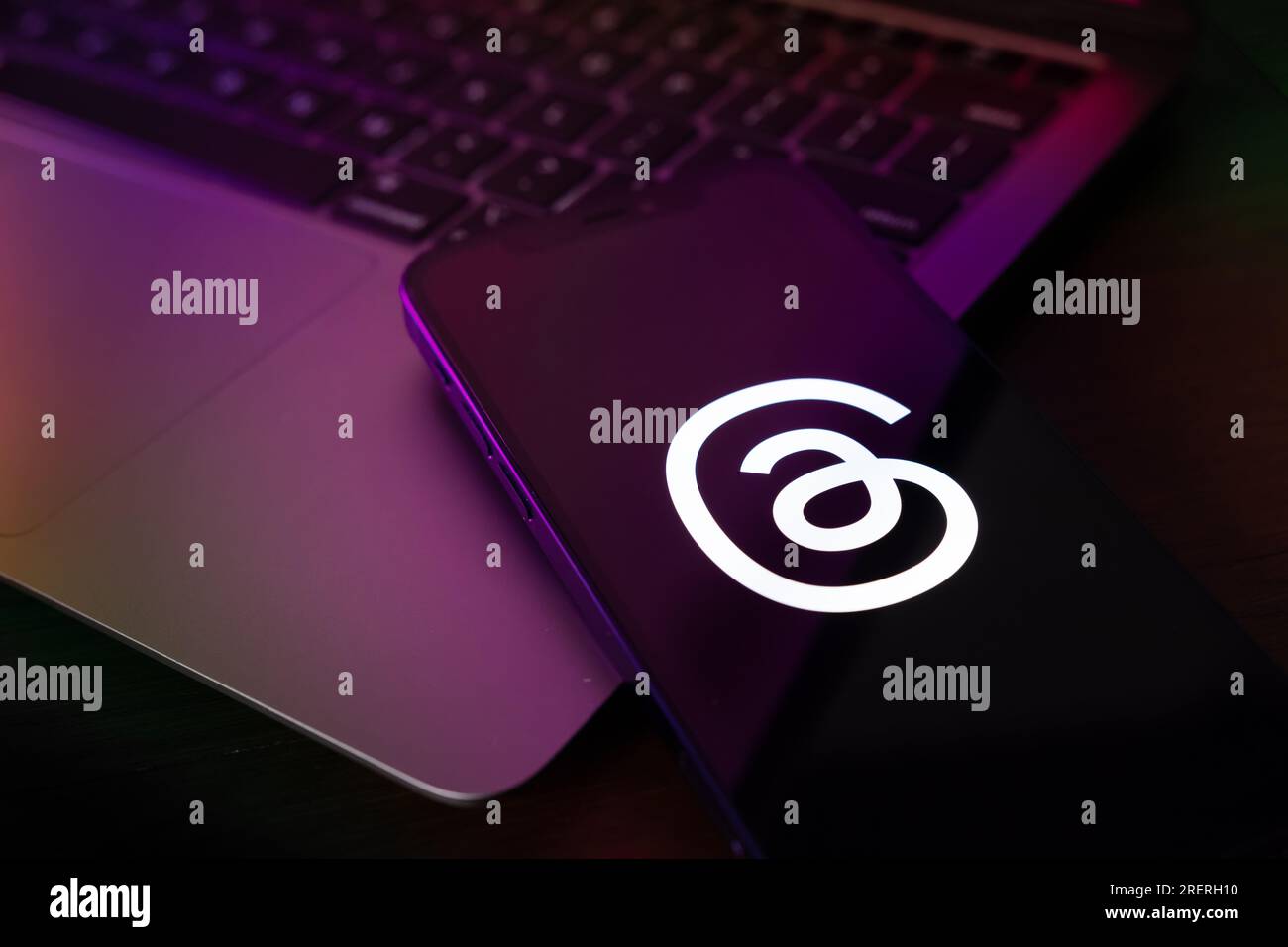 Il logo dell'app Threads viene visualizzato sullo schermo del telefono con il laptop in background Foto Stock
