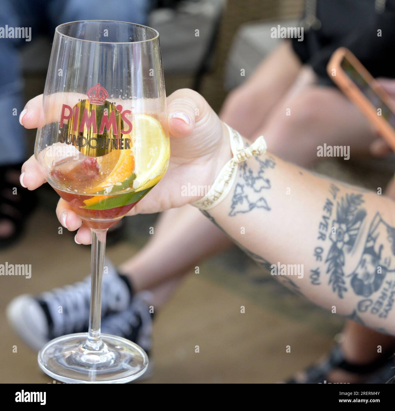 Manchester, Regno Unito, 29 luglio 2023. Una persona con tatuaggi a braccio tiene un drink in un bicchiere di Pimms al pop-up Capri Beach Bar, Exchange Square, Manchester, Regno Unito. Manchester Day - in vacanza!, gratuito, divertente, adatto alle famiglie, eventi per le strade del centro di Manchester, Regno Unito. Sostenuto dal Manchester City Council, Manchester Airport Group, Biffa, The Co-op, Manchester Evening News, Cammina sul Plank, il Regno dei dolci, il British Firefighter Challenge e il Capri Beach Club. Credito: Terry Waller/Alamy Live News Foto Stock