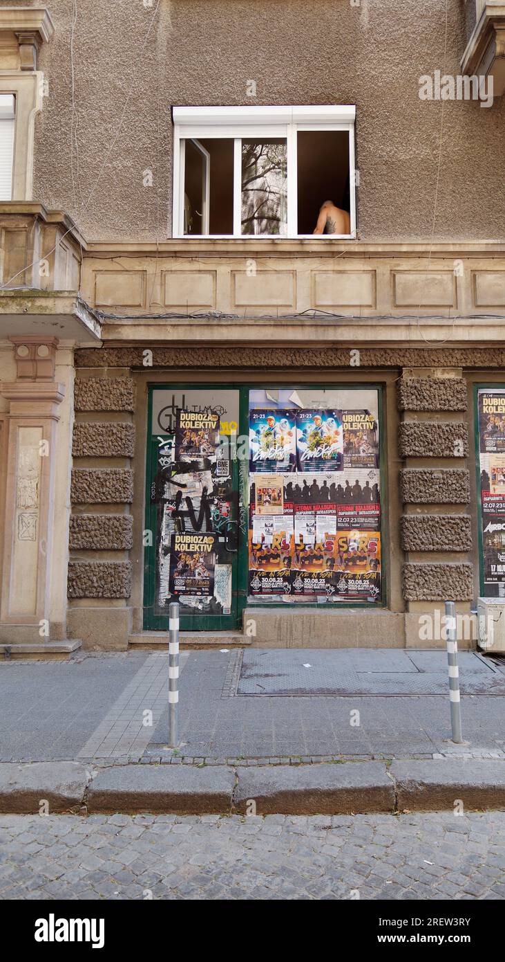 Edificio grigio con poster promozionali mentre un uomo tatuato si trova nella finestra. Sofia, Bulgaria. 29 luglio 2023 Foto Stock