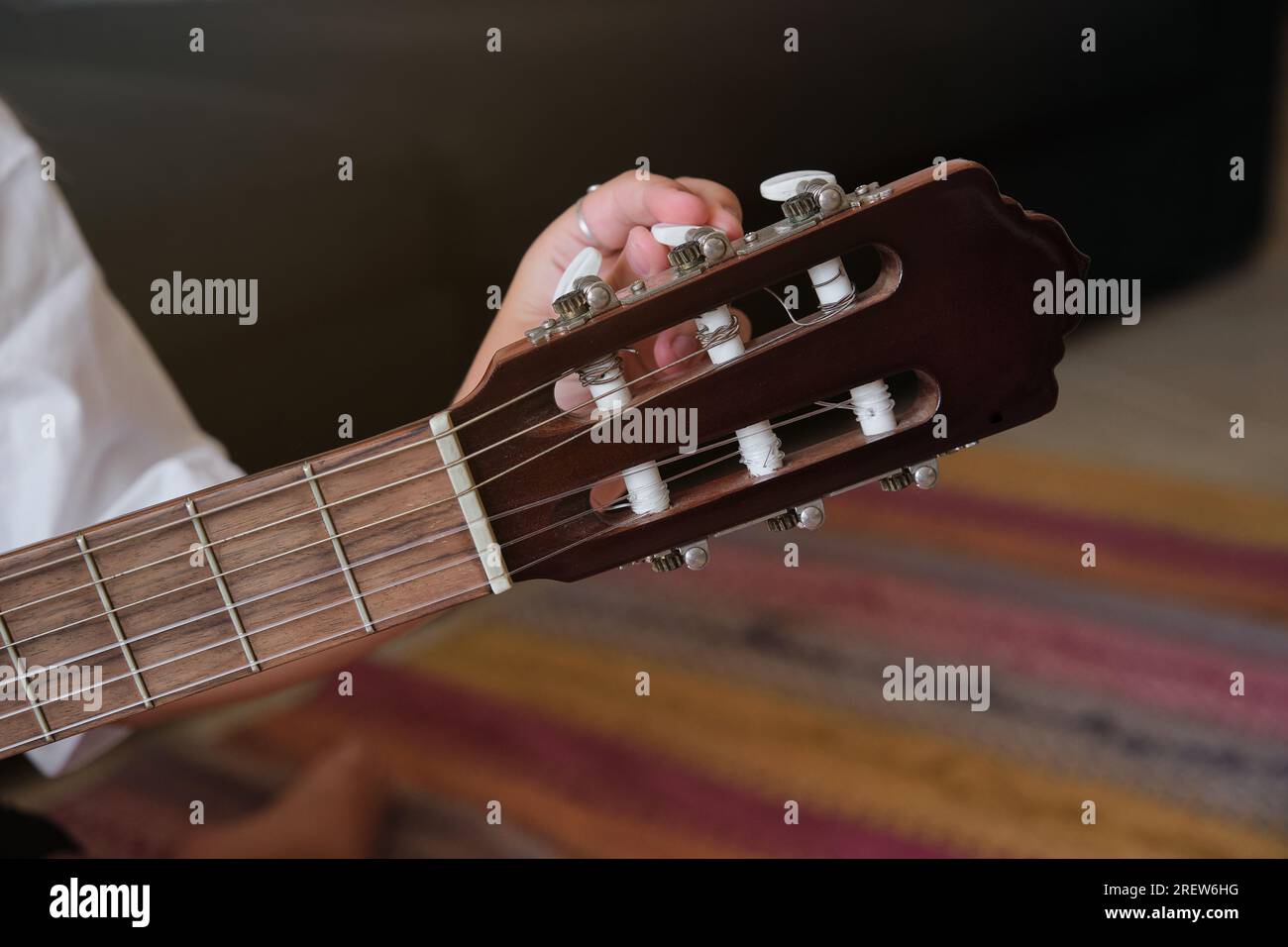 Ritaglia un musicista anonimo in abiti bianchi sintonizzando i pioli di chitarra acustica sapientemente per suonare le canzoni Foto Stock