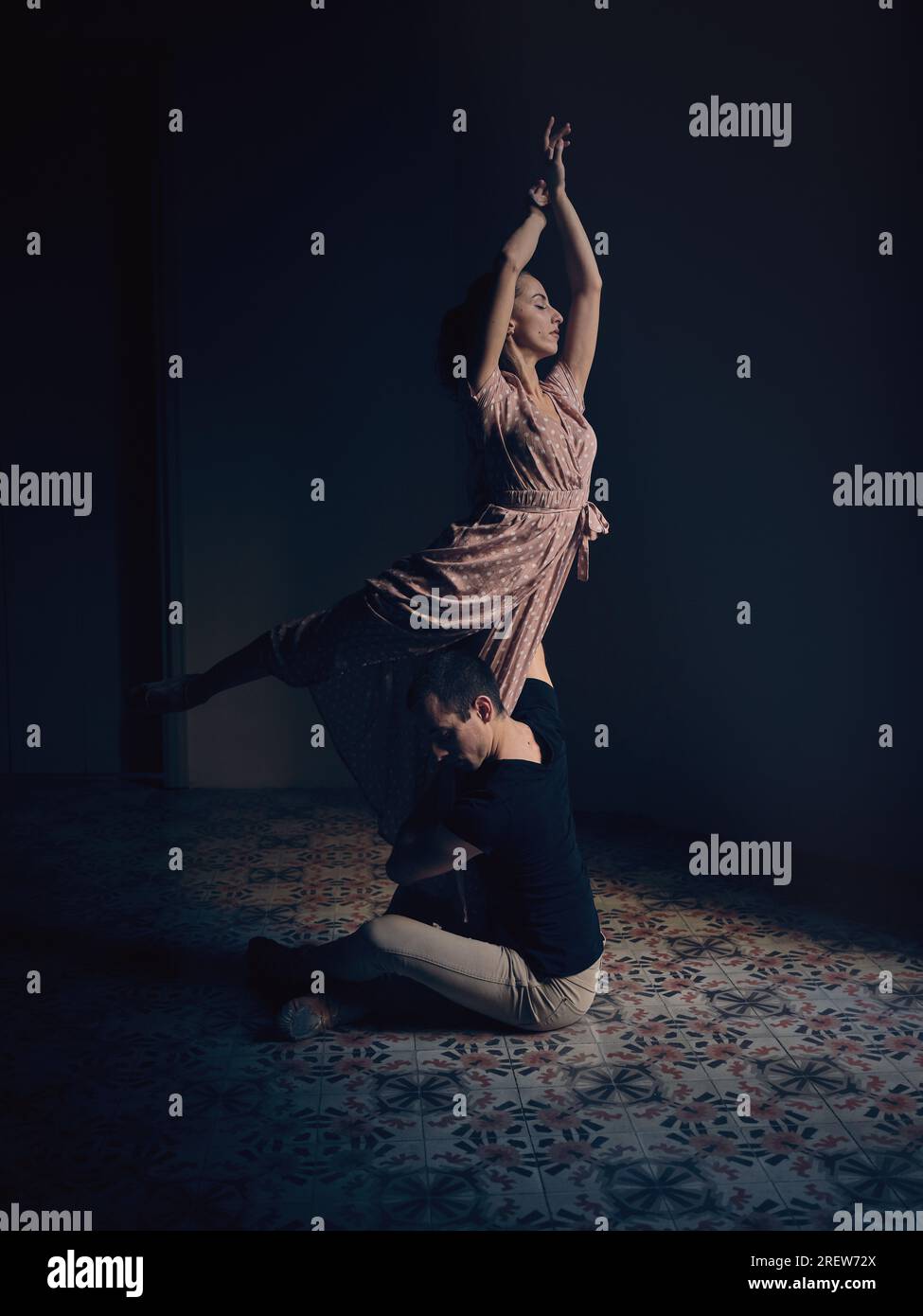 Vista laterale completa del ballerino maschile che sostiene la ballerina in piedi su una gamba mentre ballano insieme in studio buio Foto Stock