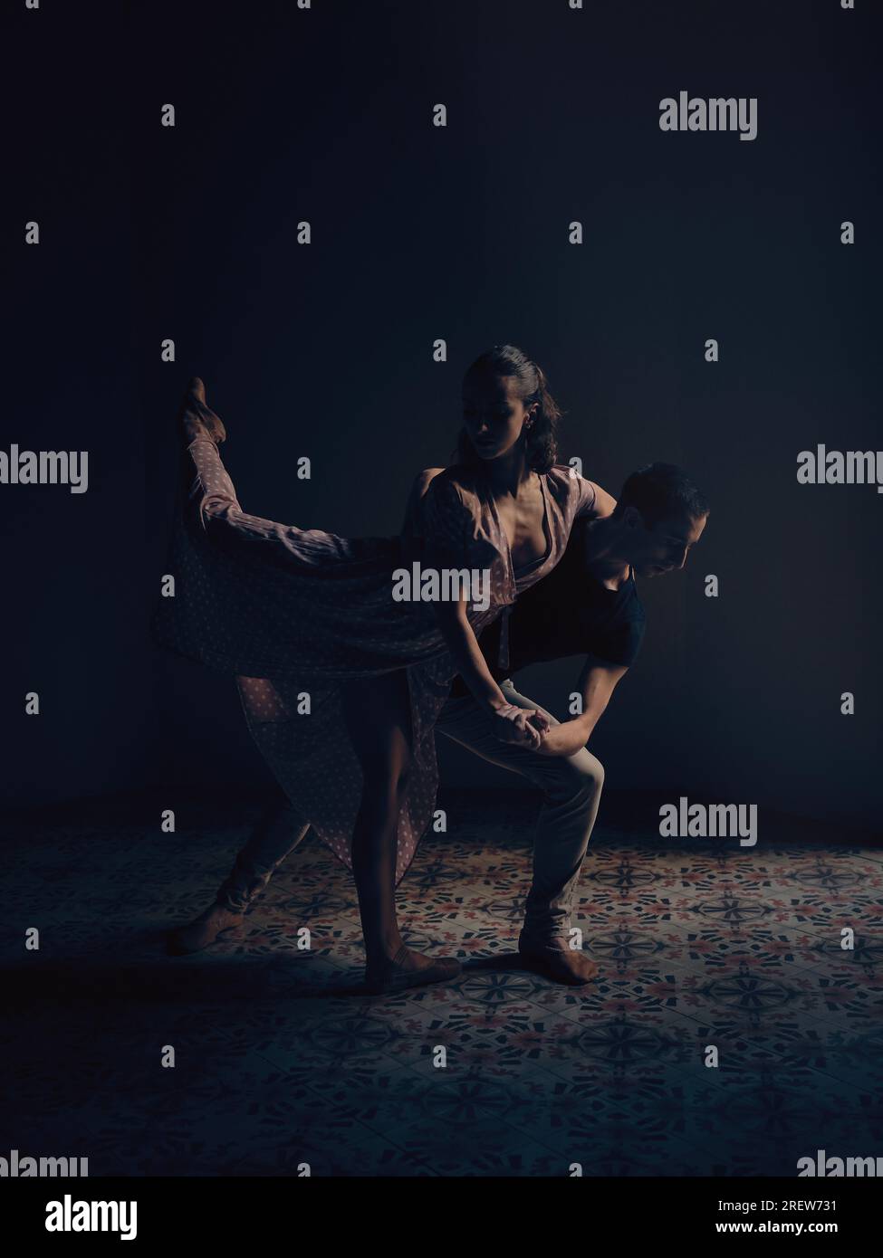 Vista laterale completa del corpo di una talentuosa ballerina in piedi con gamba sollevata mentre si appoggia all'uomo in uno studio buio Foto Stock