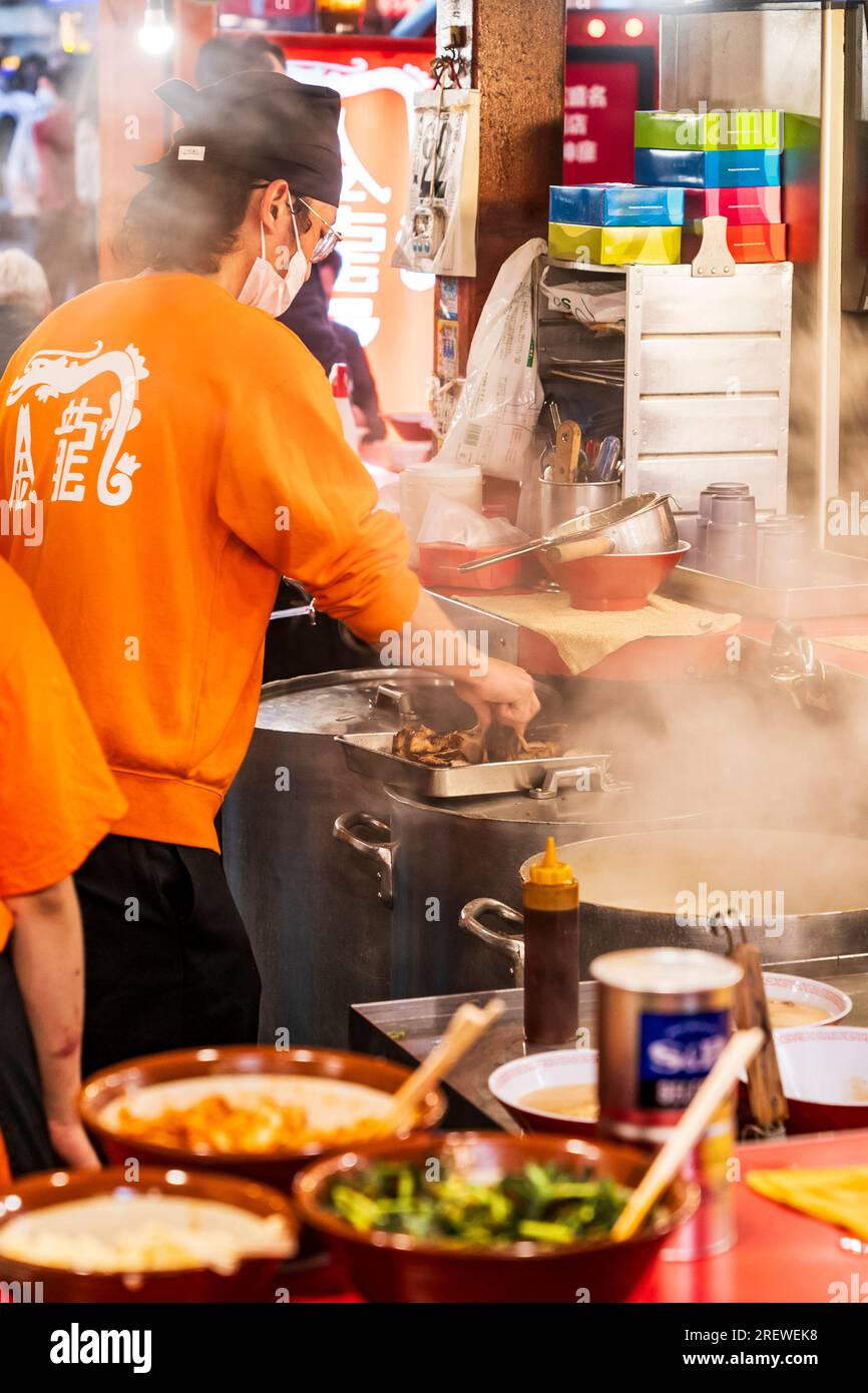 Primo piano di uno chef che cucina, tra il vapore crescente e il piano di lavoro disordinato, nel ristorante Kinryu Ramen a Dotonbori, Osaka la sera. Foto Stock