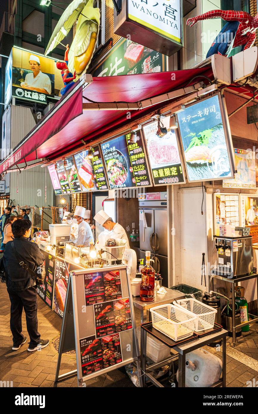 Vista notturna lungo il banco da asporto con diversi chef che servono clienti presso il popolare ristorante di manzo Wanomiya Kobe a Dotonbori, Osaka. Foto Stock