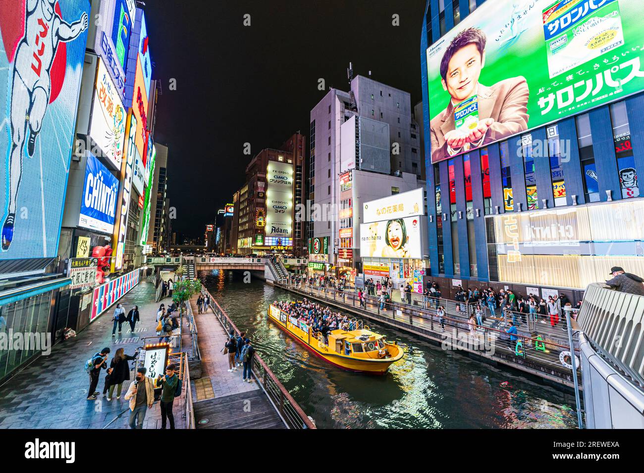 Vista dal ponte Ebisu di notte di una barca da crociera piena di turisti sul fiume con la famosa esposizione al neon Glico Running Man a Dotonbori, Osaka. Foto Stock