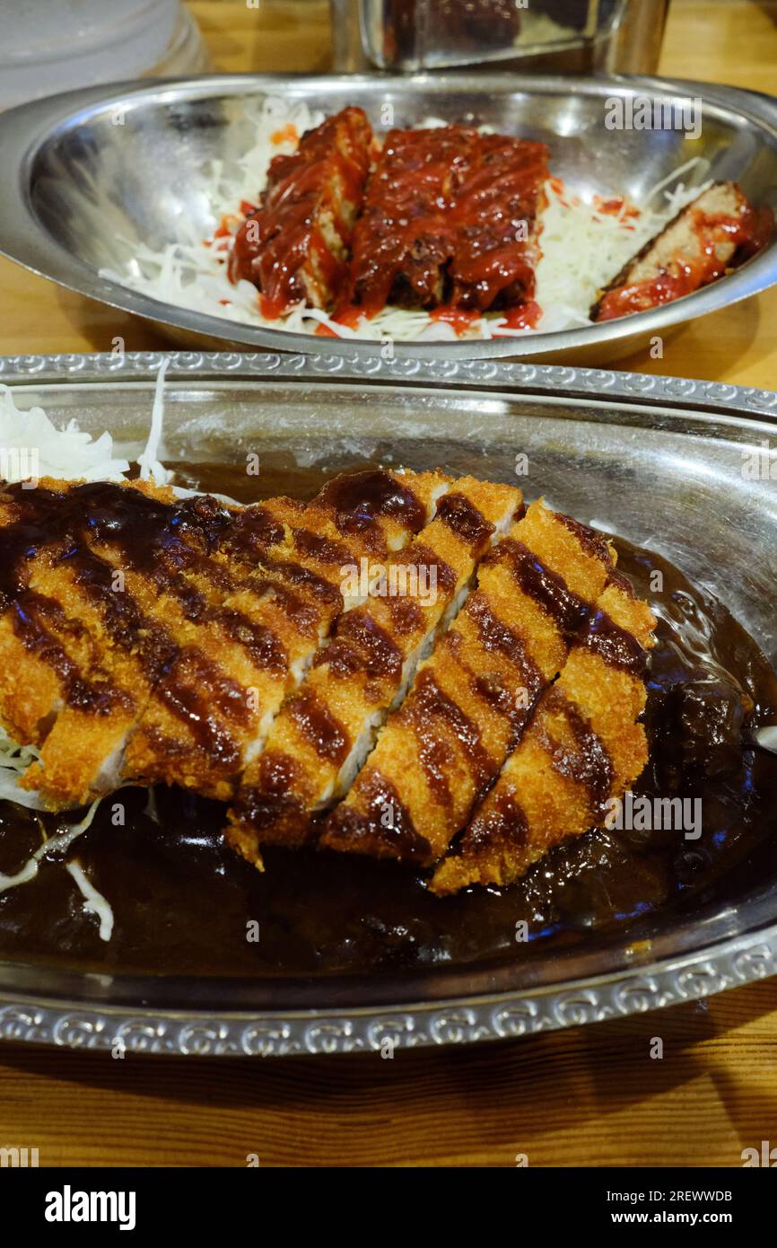 Luglio 2023, Un piatto di riso al curry giapponese con cotoletta di maiale fritta in profondità impanata (tonkatsu) e un piatto di hamburger giapponese (hambagu) sullo sfondo Foto Stock