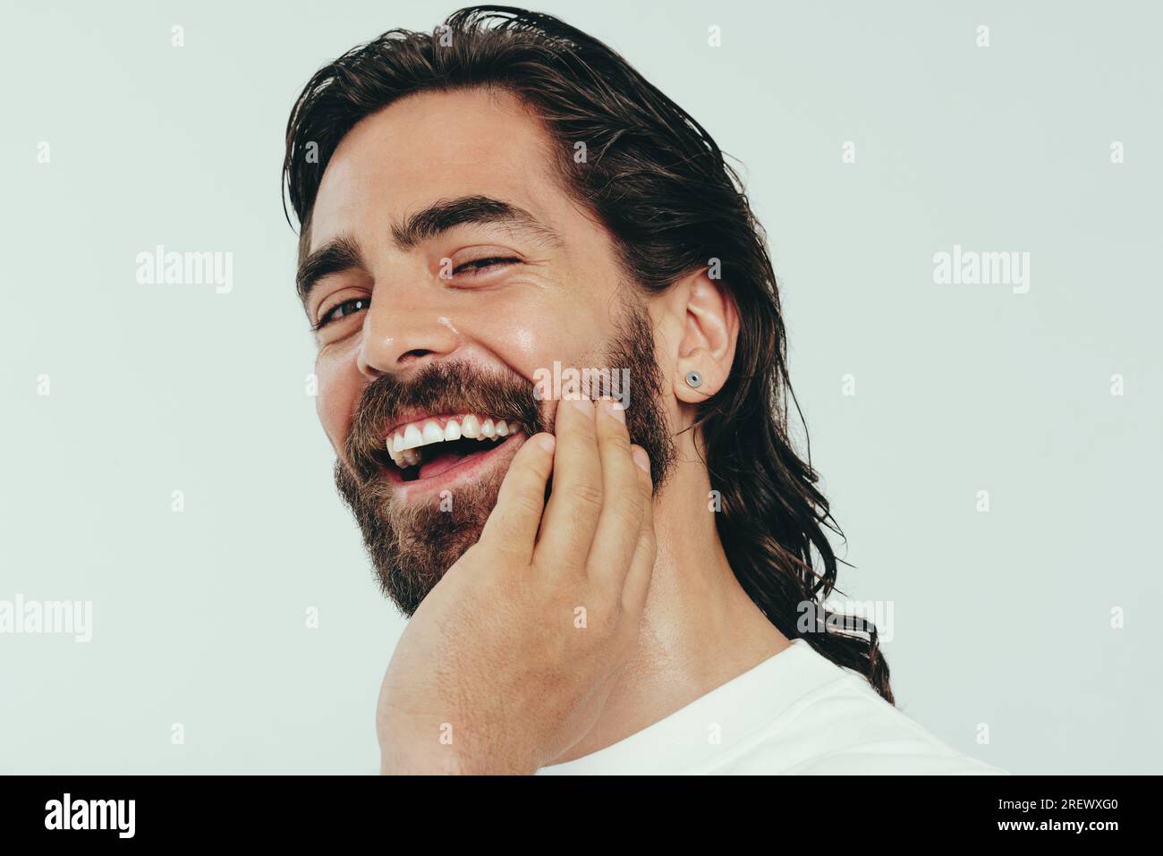 Ritratto di un giovane uomo felice sorridente in uno studio di registrazione, guardando la fotocamera con sicurezza mentre si sfreccia con orgoglio la barba, i capelli lunghi e la pelle radiosa. Uomo Foto Stock