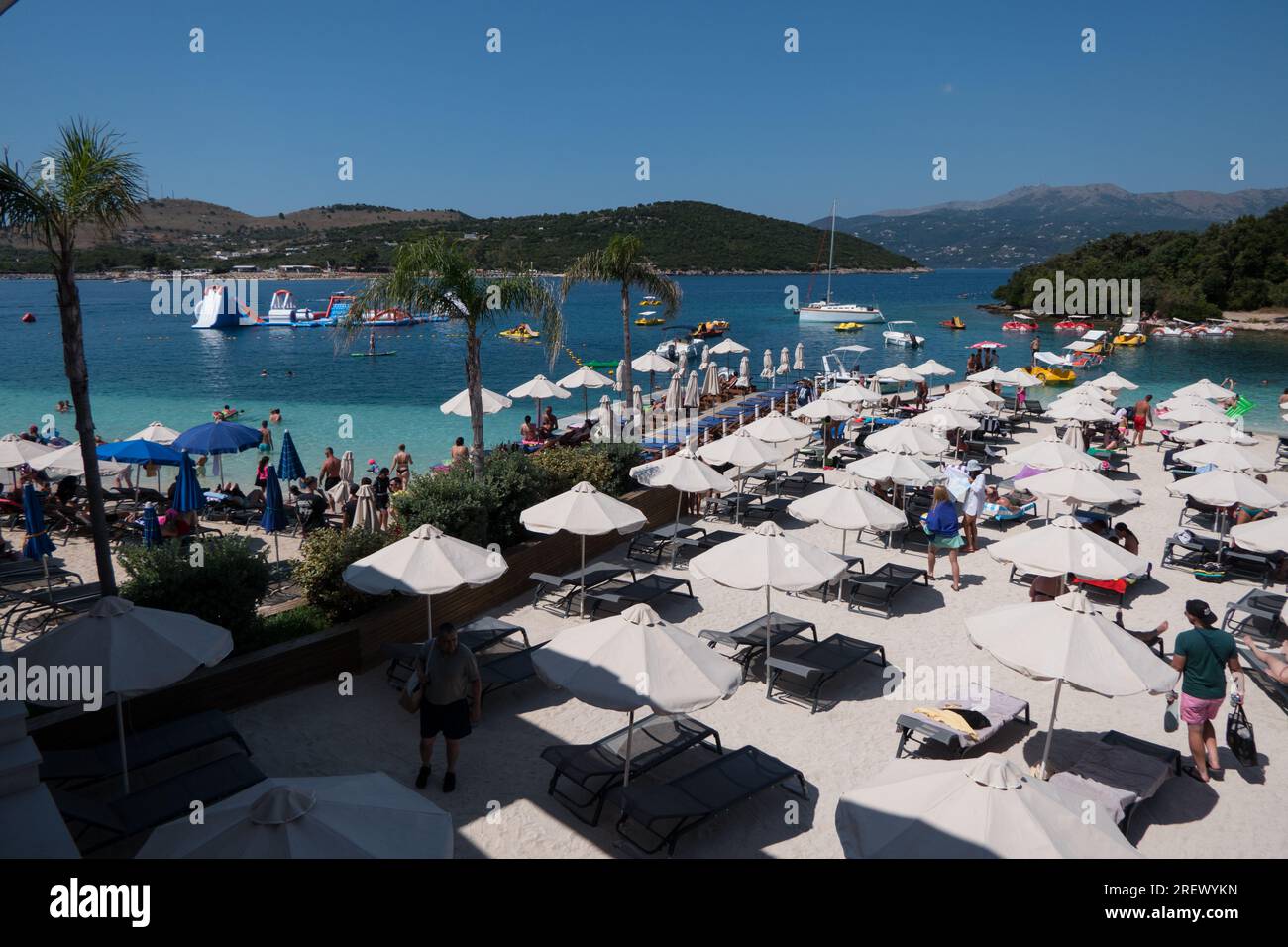 Vista della spiaggia affollata di Ksamil, Albania, con persone che nuotano e si divertono vicino al 3 resort di Ishujt. Turisti che si godono l'estate in una destinazione albanese Foto Stock