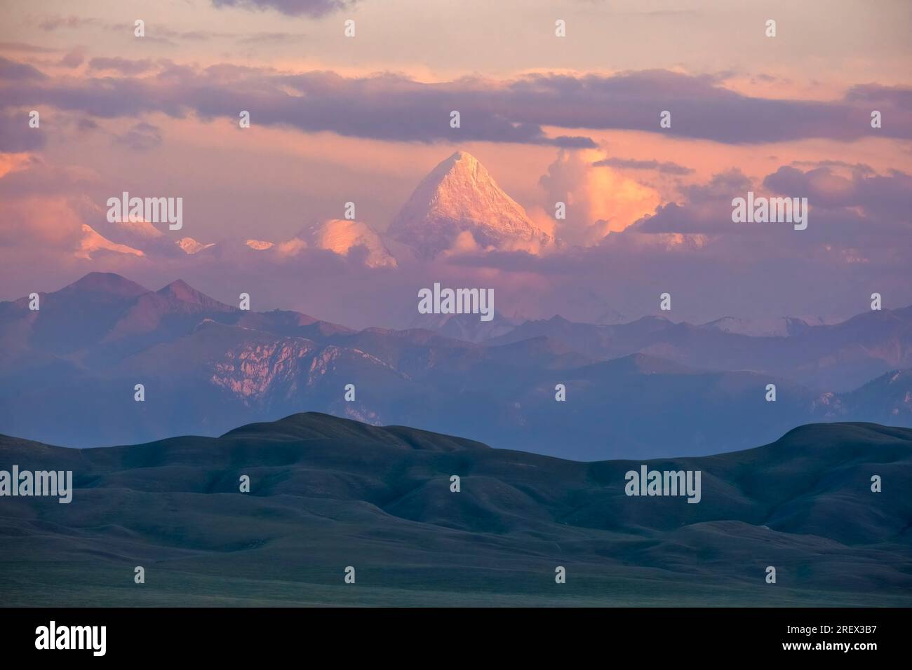 Il grande Monte Khan Tengri sorge sopra altre montagne e catene montuose durante un'alba rosa Foto Stock