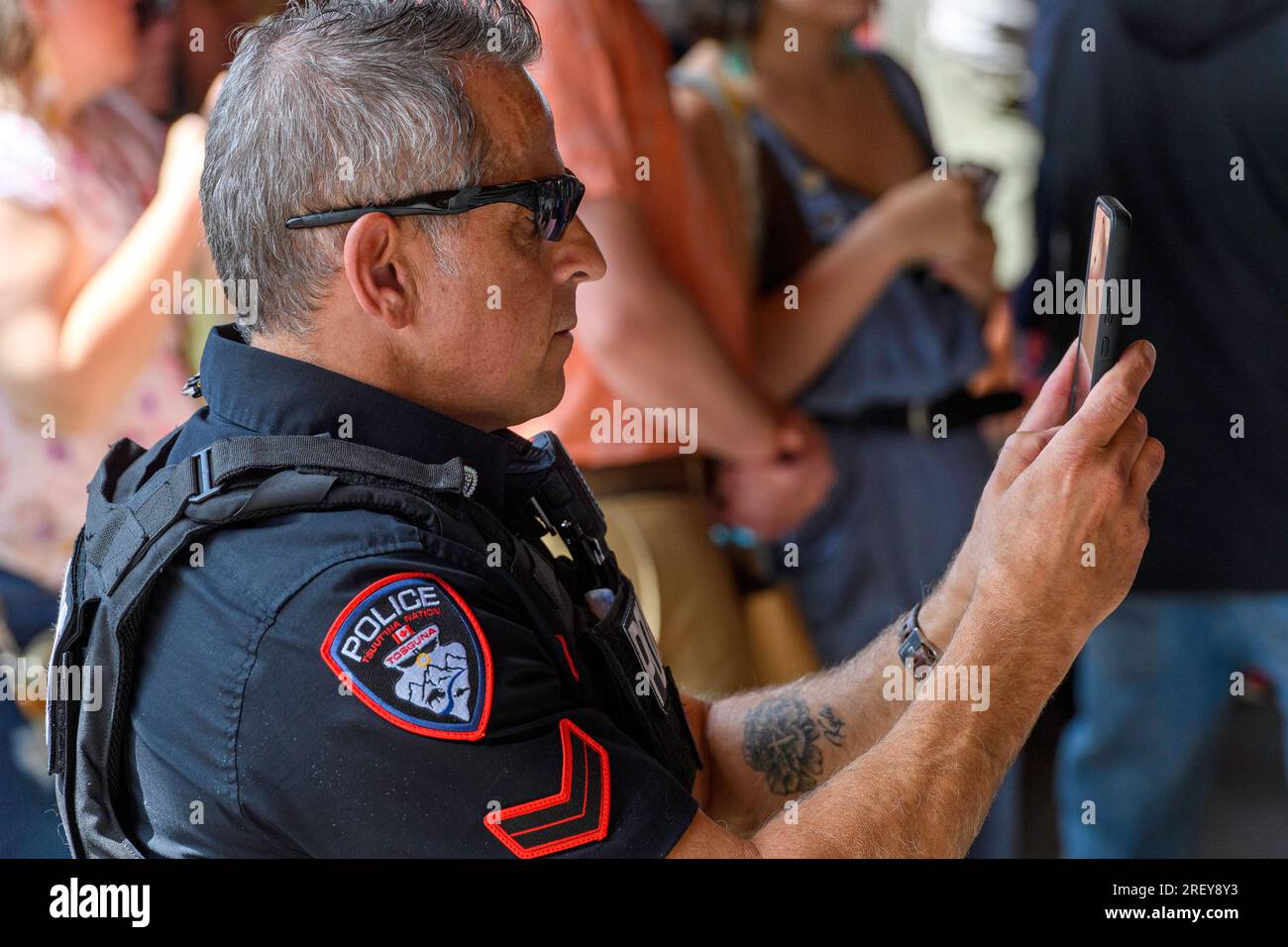 Un agente di polizia di Tsuut'ina Nation che partecipa alla cerimonia di ingresso Grand Powwow a Bragg Creek, Alberta, Canada, mentre la filma su uno smartphone. Foto Stock