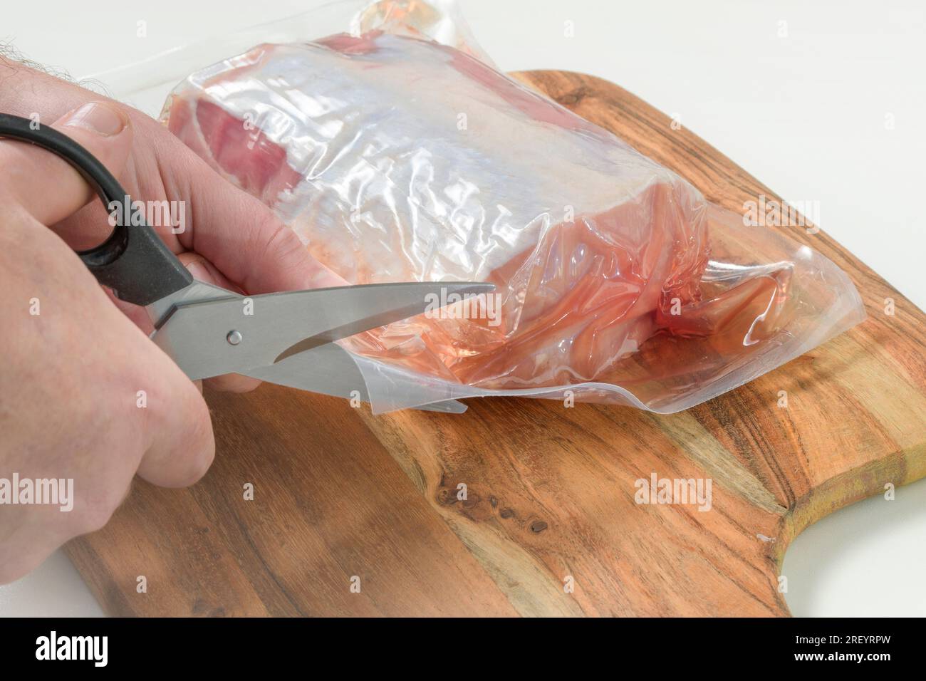 Tagliare con le forbici l'imballaggio sottovuoto con la carne. Rimuovere il pezzo di carne dalla confezione sottovuoto in plastica Foto Stock