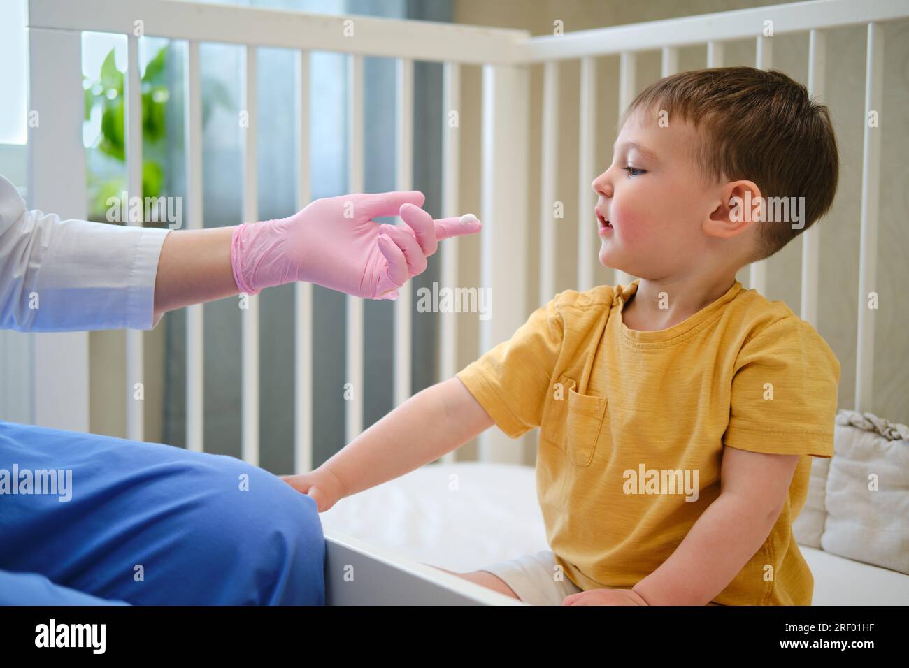 Il medico sta usando un idratante sul viso del bambino infantile per trattare l'eczema. Bambino di circa due anni (un anno e undici mesi) Foto Stock