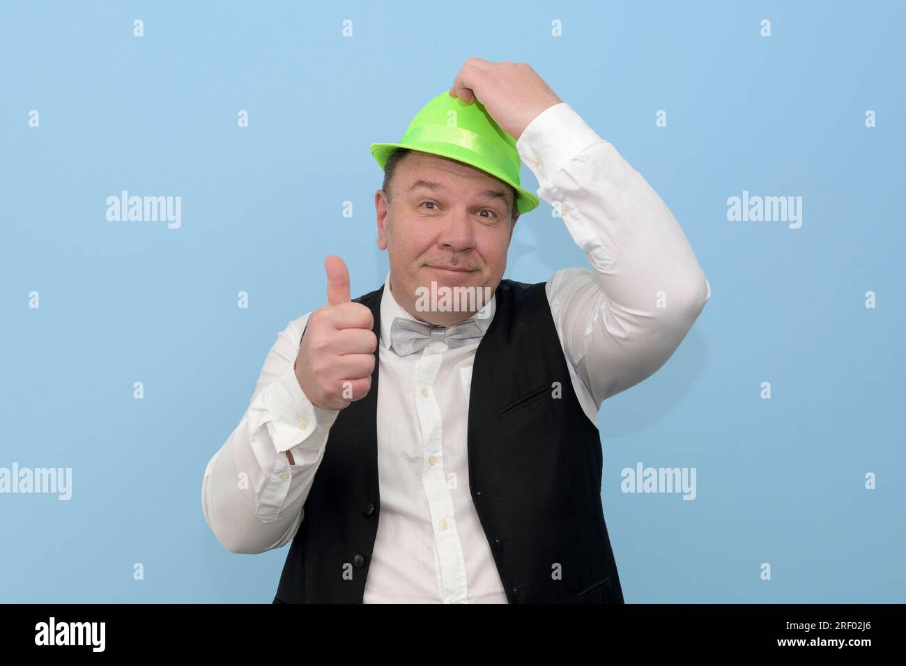 Bella festa. Un uomo di mezza età con un cappello verde di carnevale ti invita a una festa. sfondo azzurro. Foto Stock
