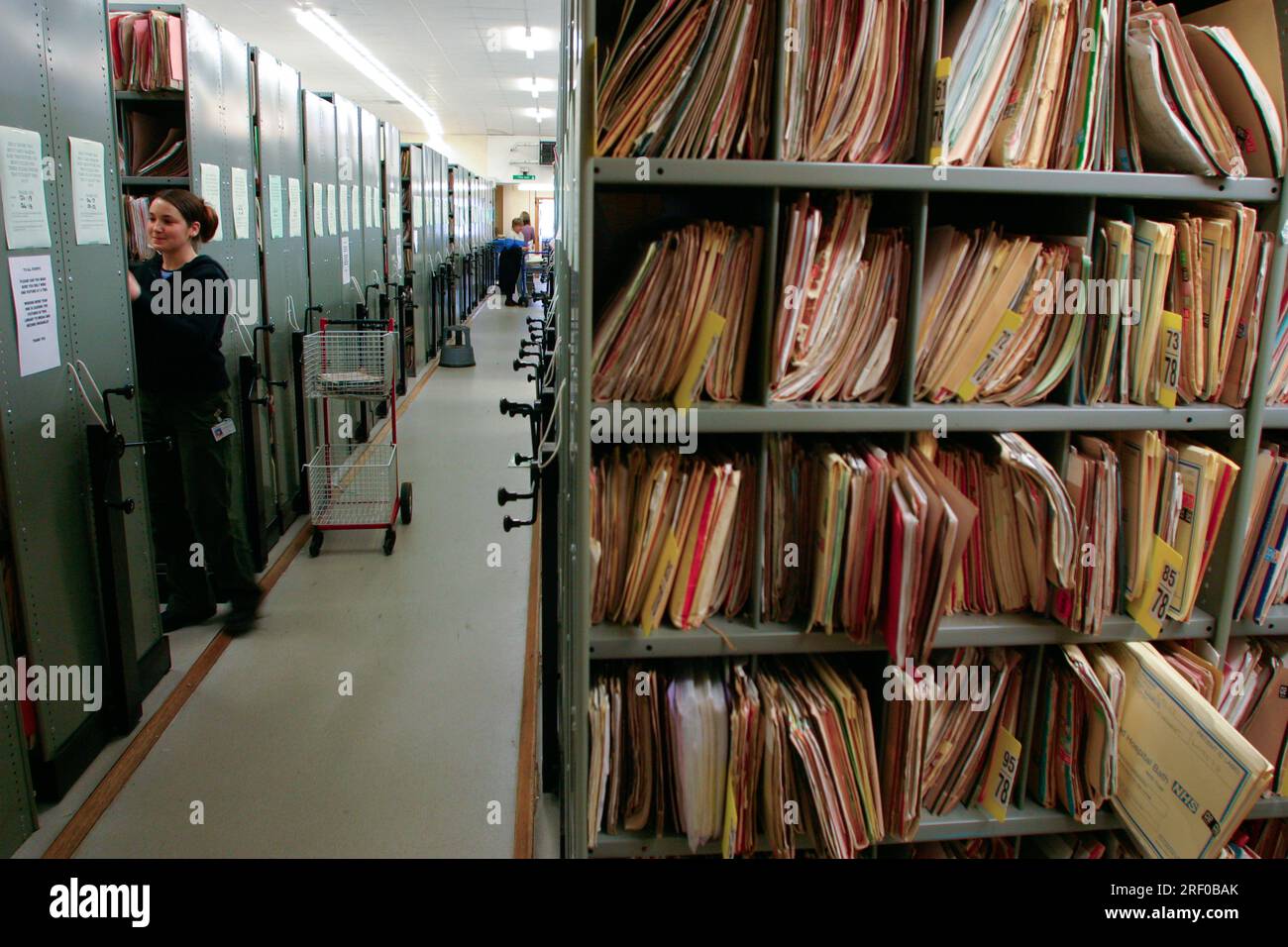 Una persona organizza i file in una grande sala archivio con file di scaffali in Inghilterra. Foto Stock