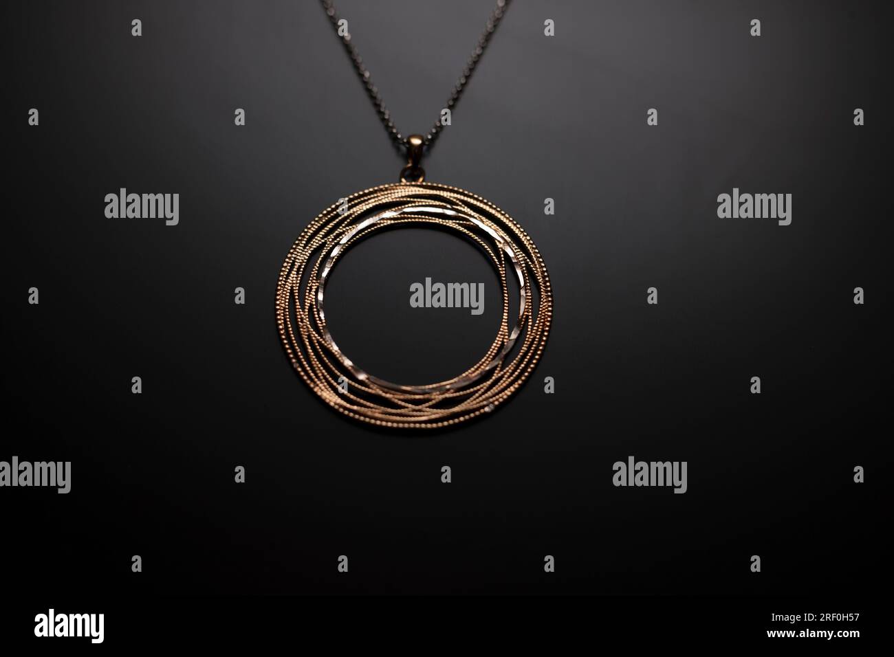 Un gioiello adagiato su uno sfondo nero leggermente illuminato. Fili e perline dorati che formano anelli. Collana in oro intrecciata a cerchi. Foto Stock
