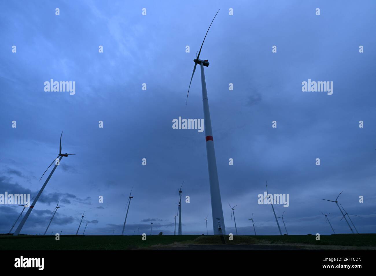 Westhausen, Germania. 31 luglio 2023. All'alba, le nuvole di pioggia passano sopra un parco eolico vicino a Westhausen. Qui sono in funzione più di 60 turbine eoliche. Nei paesi del nord e dell'est, ora si genera più energia eolica di quanto si consuma lì. Poiché la rete elettrica deve essere ampliata a grandi spese per trasportarla a sud, le tariffe di rete che sono state addebitate a livello regionale fino ad ora stanno aumentando. Credito: Martin Schutt/dpa/Alamy Live News Foto Stock