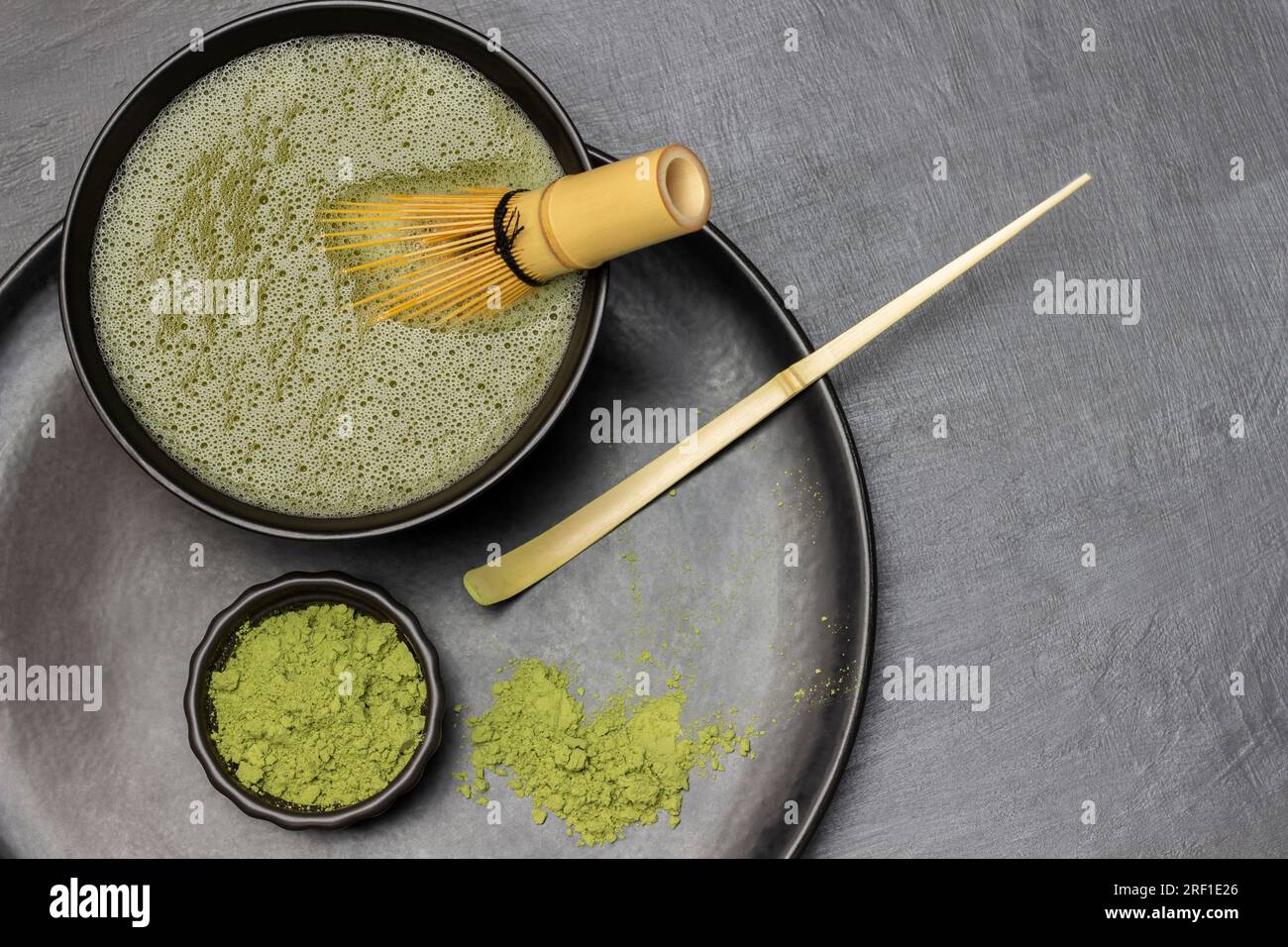 Misurino e tè matcha in polvere, frusta di bambù in un recipiente con tè matcha. Spianatura piatta. Copia spazio. Sfondo grigio. Foto Stock