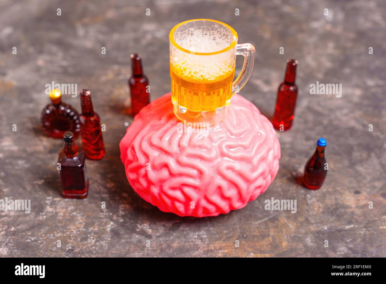 Un bicchiere da birra giocattolo posto sopra un modello di cervello umano circondato da una selezione di liquori e bottiglie di birra. Rompere il circolo vizioso di stress e alcoholi Foto Stock