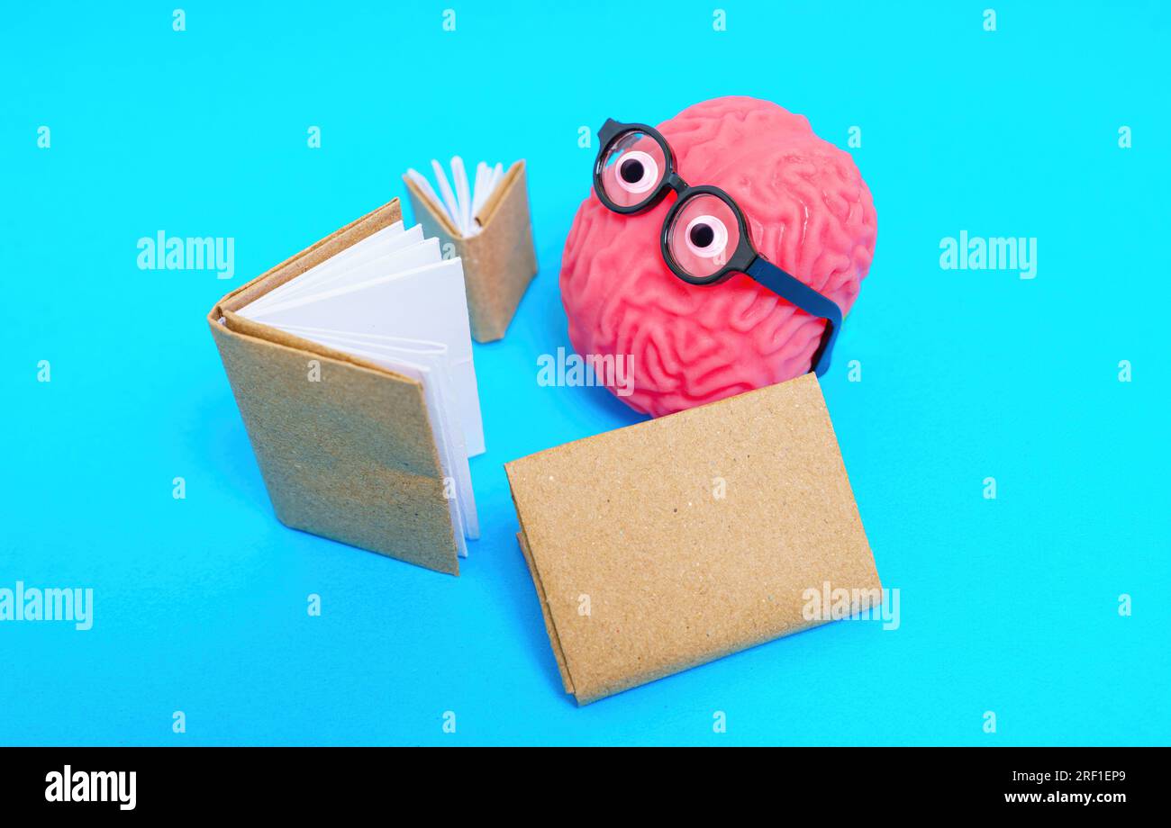 Primo piano di un simpatico personaggio realizzato con un modello cerebrale umano e occhi goocchi con occhiali legge libri isolati su sfondo blu. Gioia dell'istruzione e.. Foto Stock