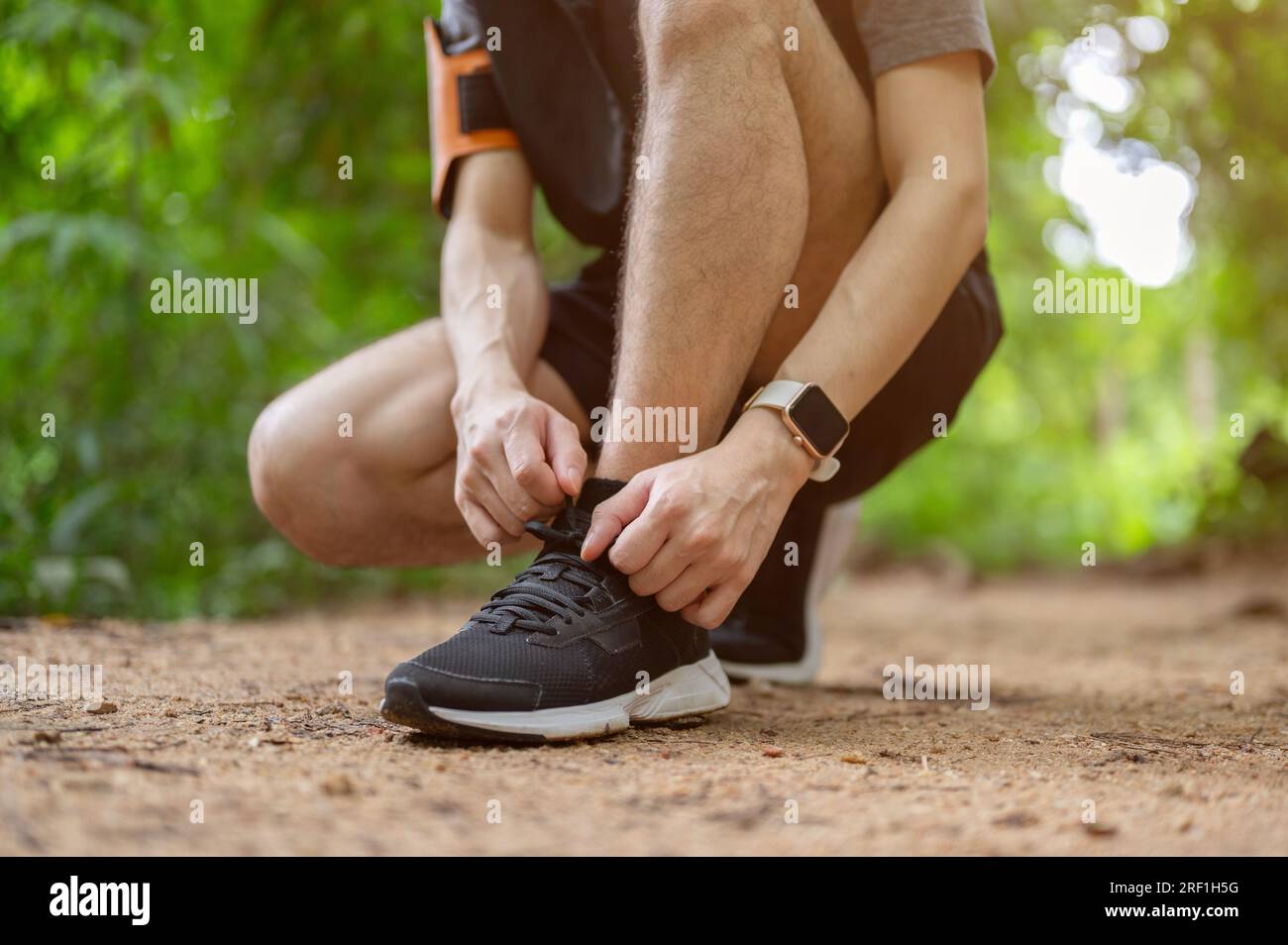 Immagine ravvicinata di un giovane asiatico sportivo e attivo che indossa abbigliamento sportivo che si lega i lacci delle scarpe mentre corre nella foresta verde. Foto Stock