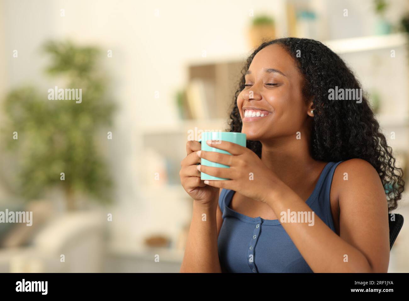 Felice donna nera che respira bevendo caffè seduta a casa Foto Stock
