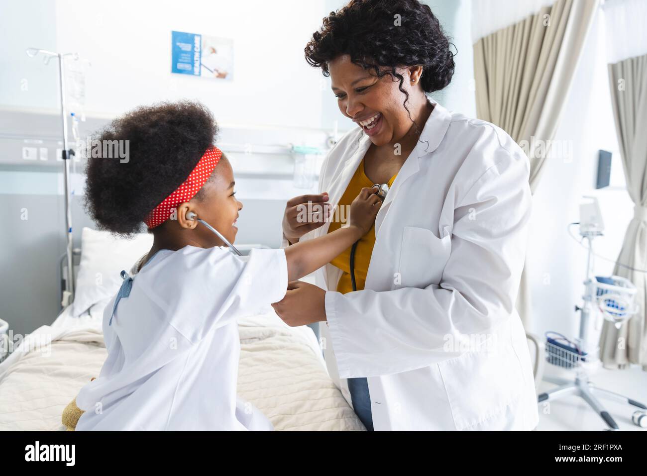 Medico donna afroamericano che gioca con paziente ragazza utilizzando stetoscopio in ospedale Foto Stock