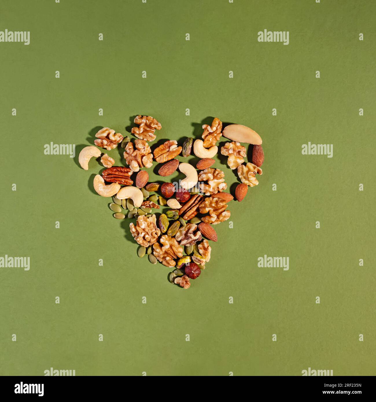 Noci miste disposte a forma di cuore su sfondo verde, concetto di dieta per la salute del cuore Foto Stock