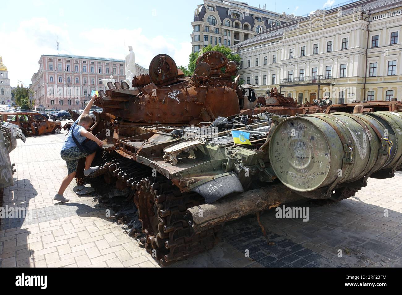 Un ragazzo clim su un carro armato dell'esercito russo estrolato è esposto in una piazza nel centro di Kiev, in Ucraina Foto Stock