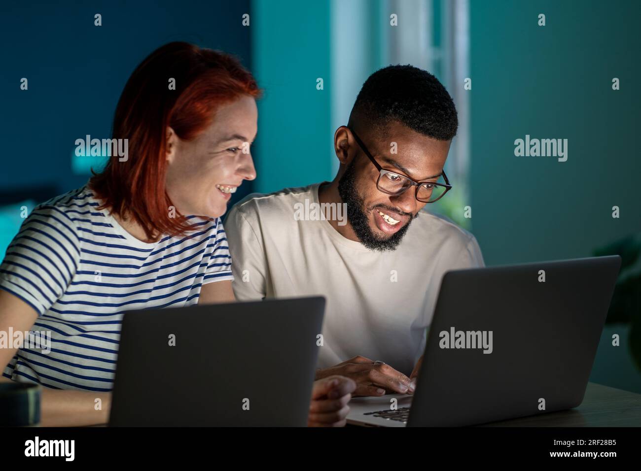 Coppia felice e diversificata ha piccole attività online al lavoro a casa con i laptop la sera Foto Stock